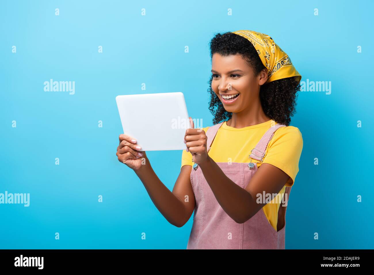 cheerful african american woman in headscarf using digital tablet on ...