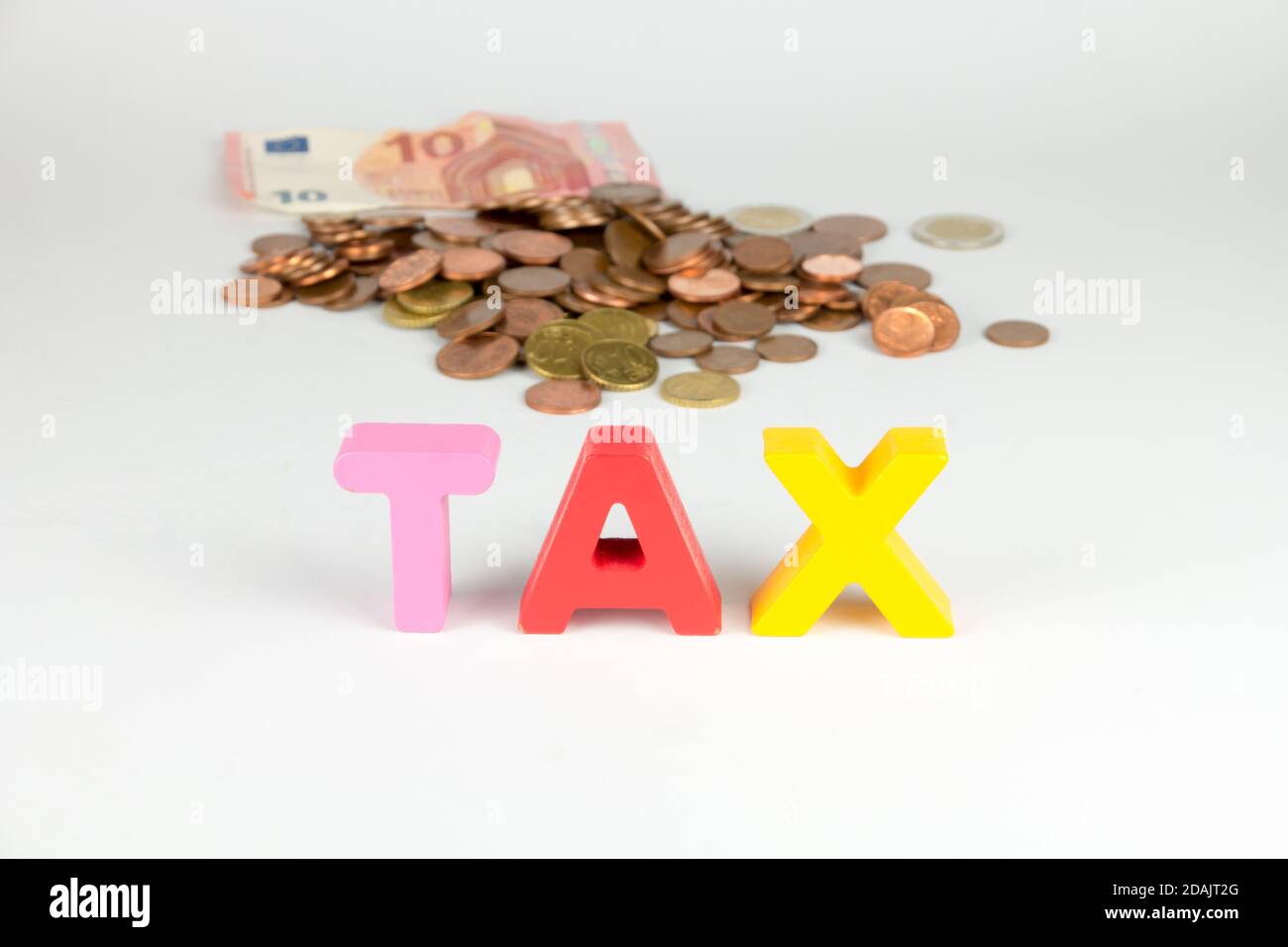 Tax paying. Sign tax with Euro coins and banknote behind it on white background. Tax payment concept. Stock Photo