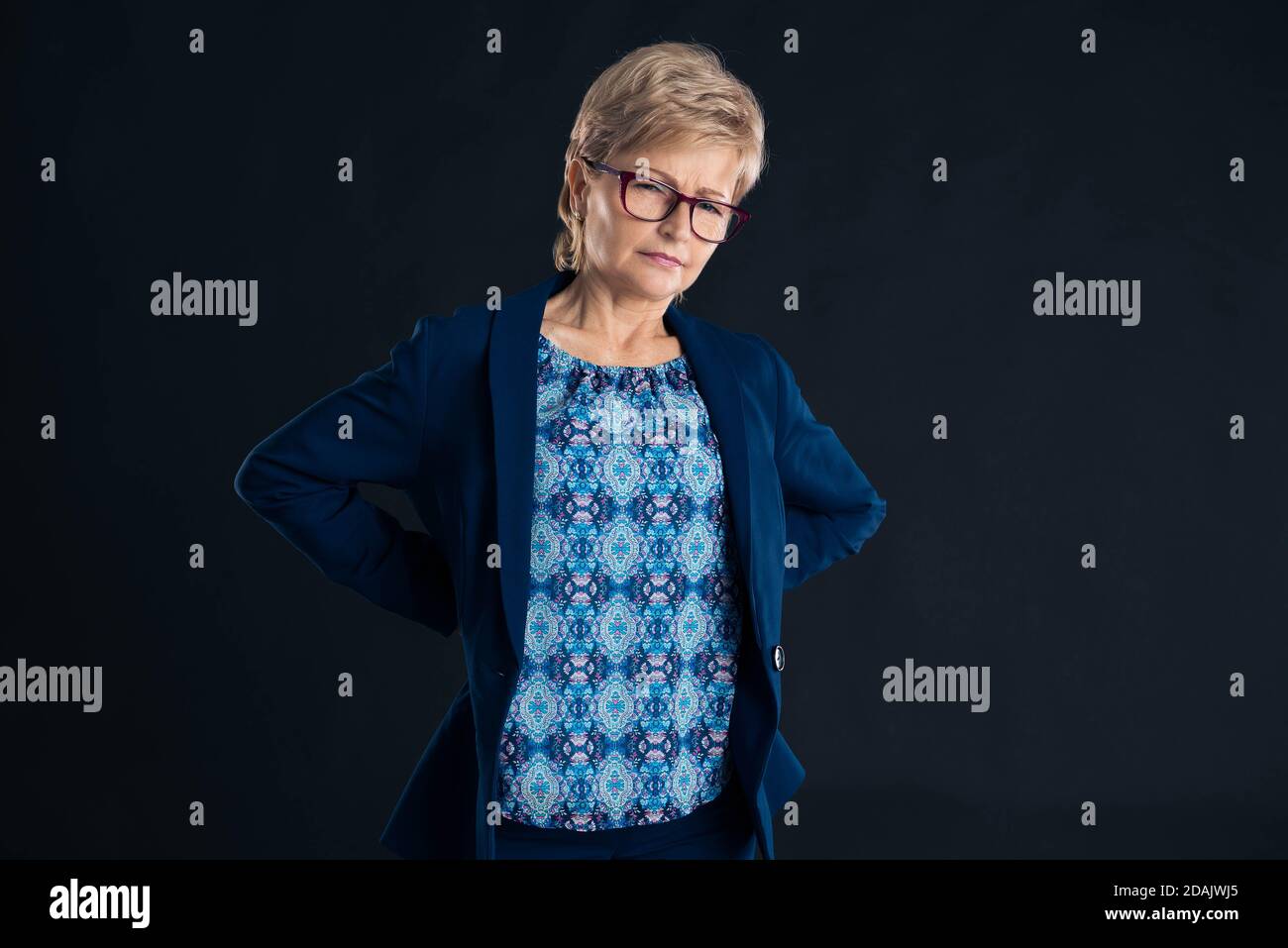 Older businesswoman having lower back pain from sitting down too much wearing a blue jacket Stock Photo