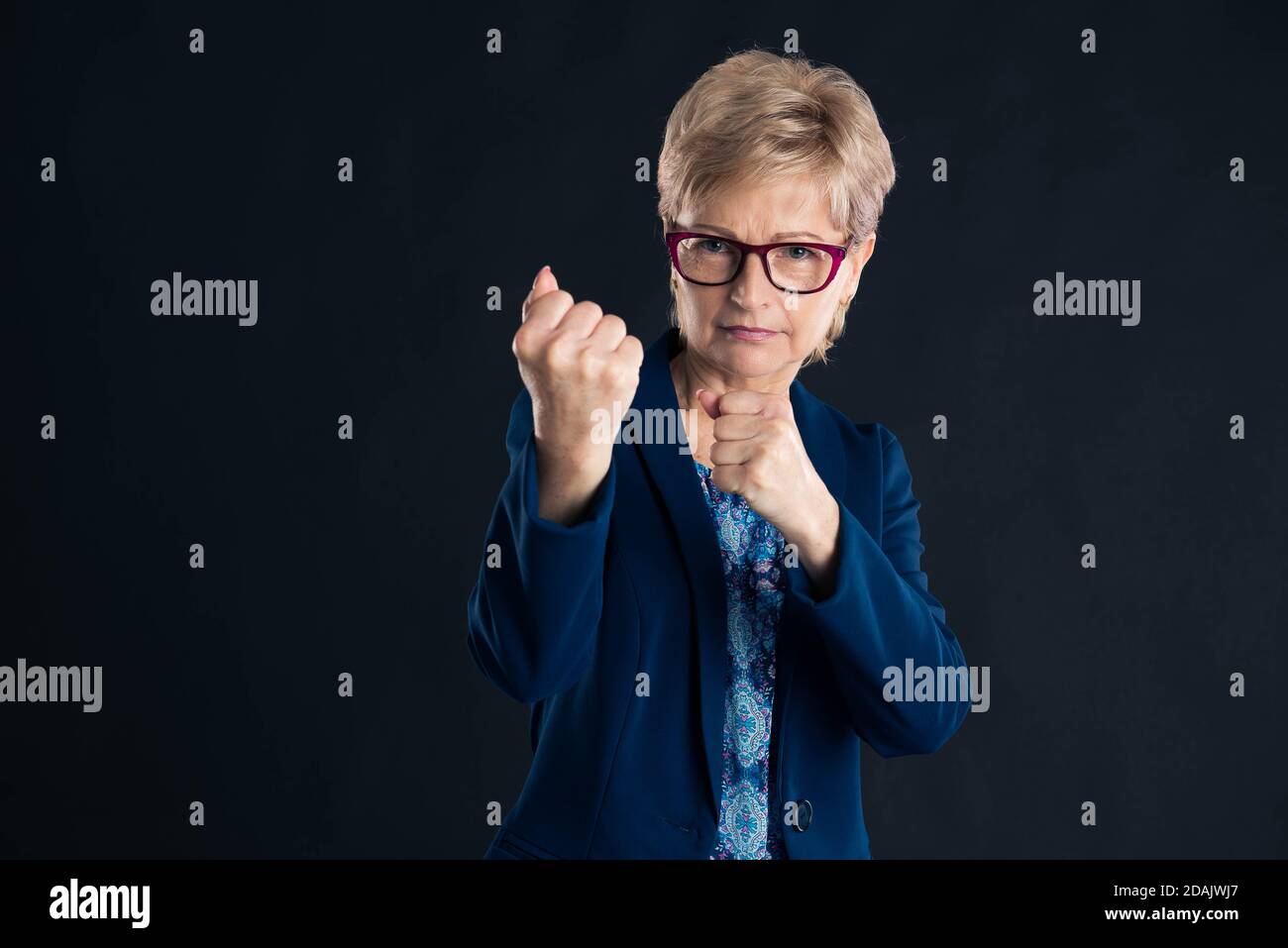 Older blonde businesswoman wants to fight you wearing glasses and a blue jacket Stock Photo