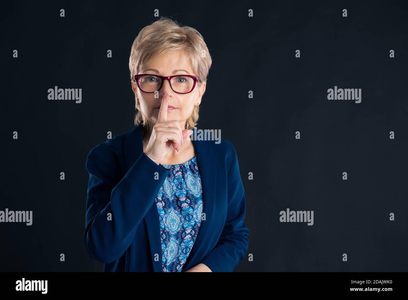 Senior secretary making silence gesture on a dark background Stock Photo