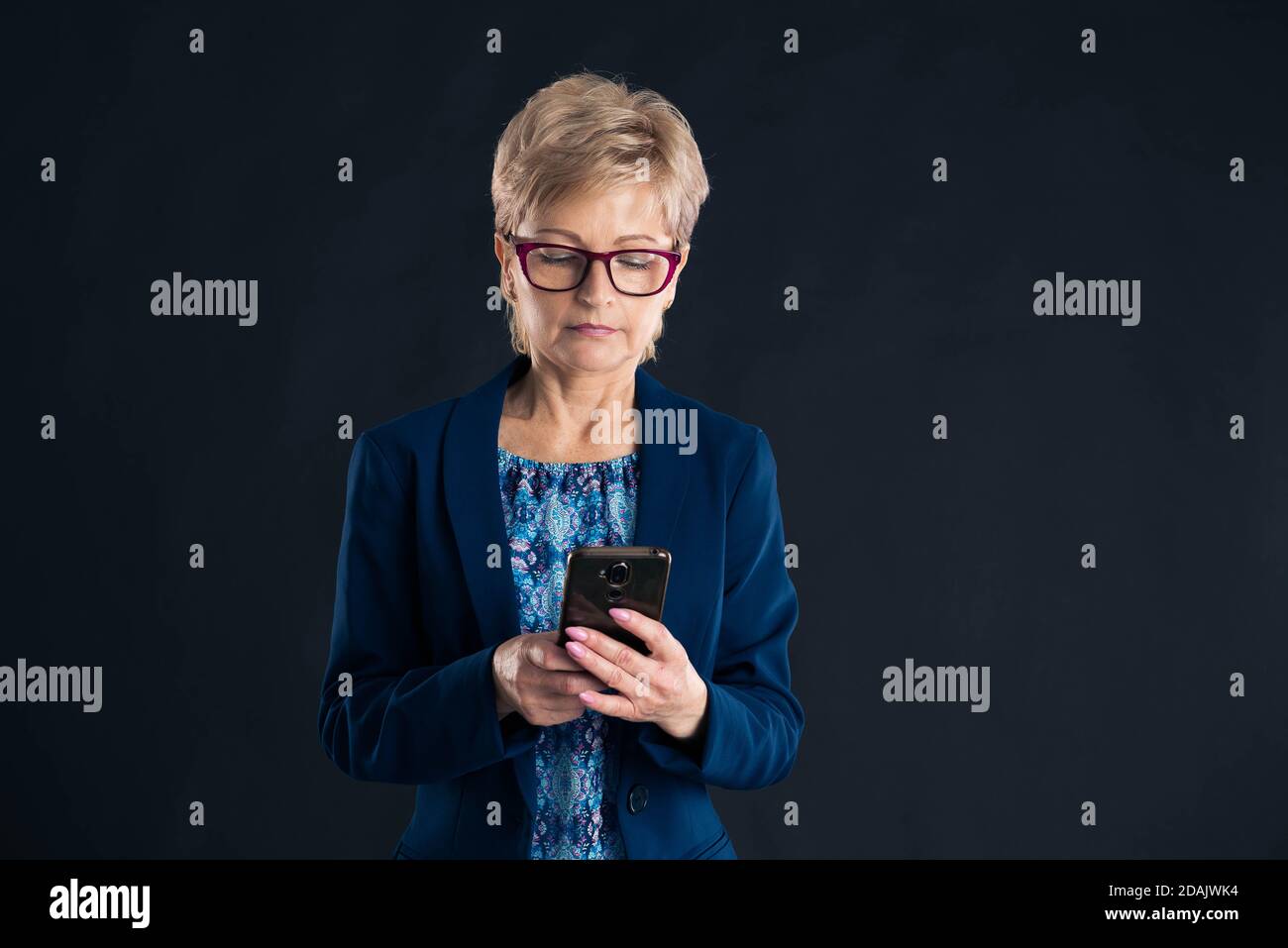 Older businesswoman texting on her mobile phone on a dark background Stock Photo