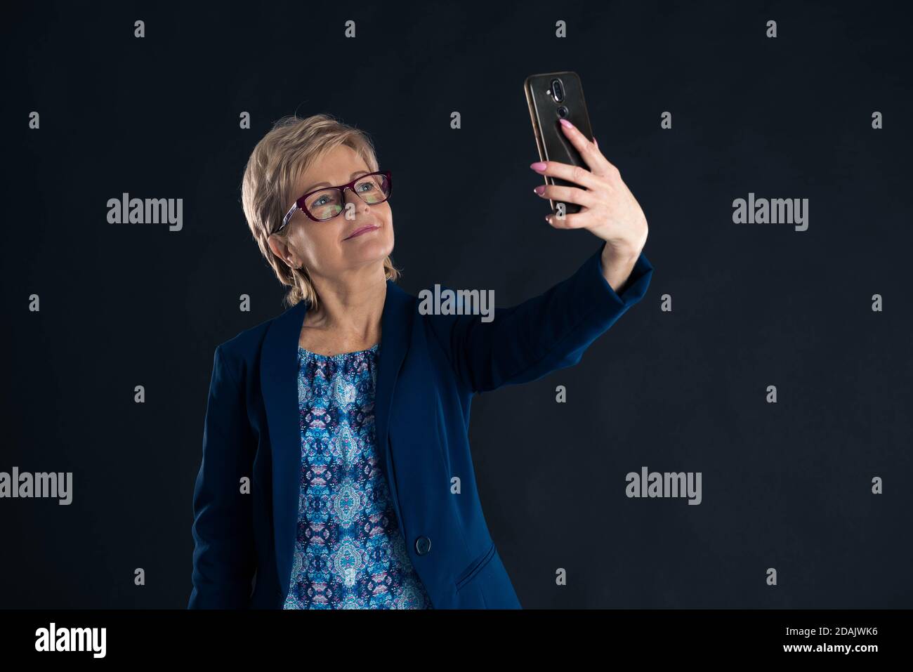 Older businesswoman taking a selfie on a dark background Stock Photo