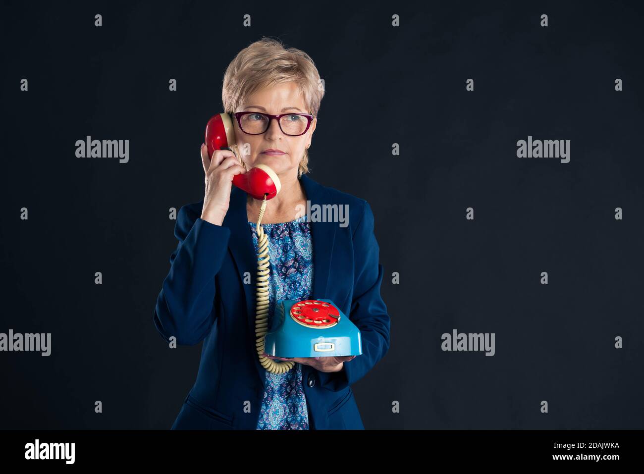 Older businesswoman talking on the telephone on a dark background Stock Photo