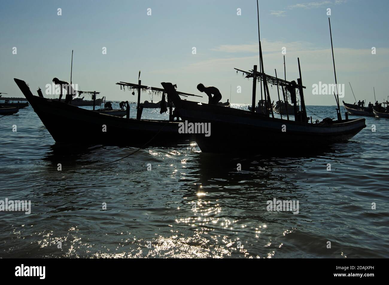 Silhouettes of Burmese fishermen ready their fishing boats for a nights fishing as the sun goes down on Ngapali beach Myanmar Stock Photo