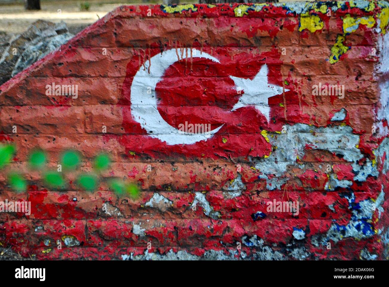Flag of Turkey painted on old brick wall with blurred green leaves. Nationalism or patriotism concept. Close up angle. Stock Photo