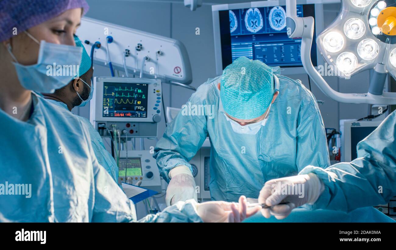 Diverse Team of Professional Surgeons Performing Invasive Surgery on a Patient in the Hospital Operating Room. Nurse Hands Out Instruments to surgeon Stock Photo