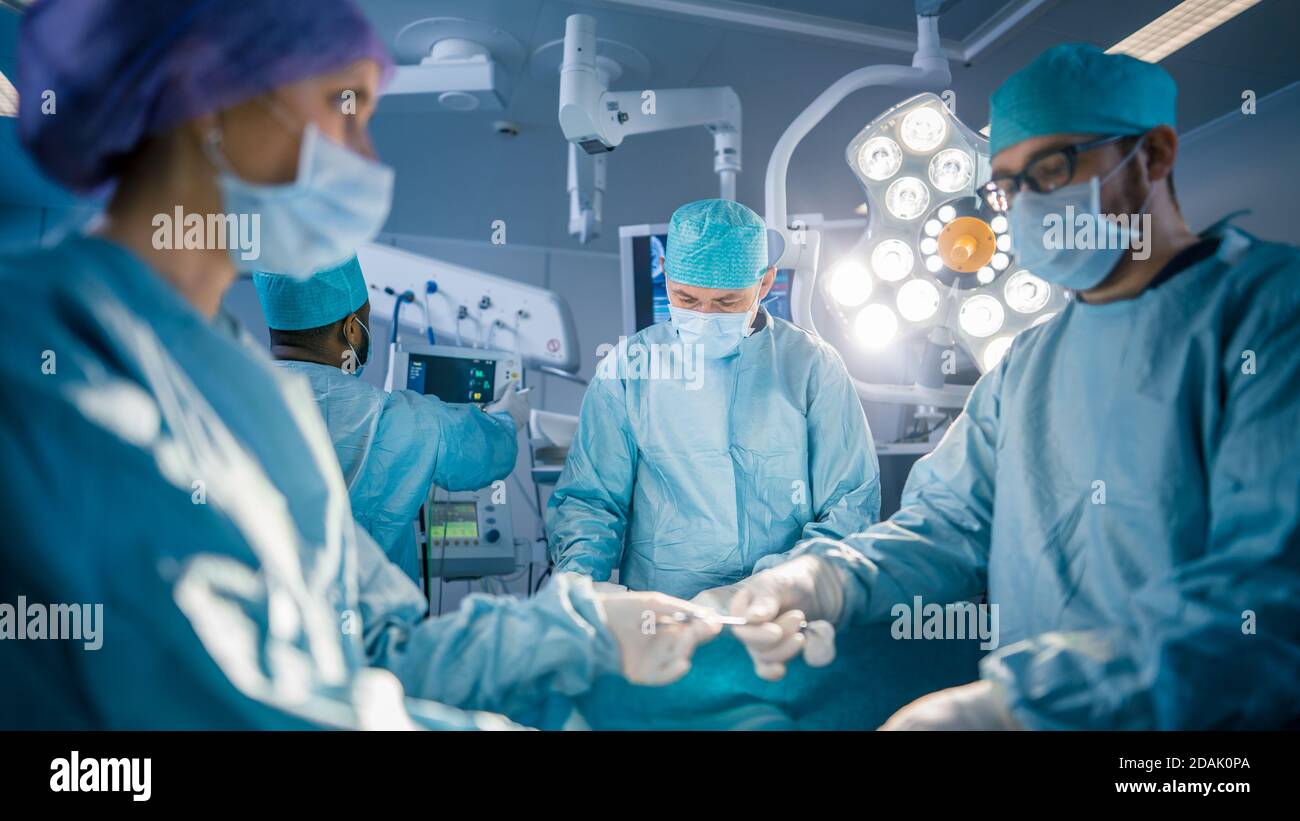 Shot in the Operating Room Assistant Hands out Instruments to Surgeons During Operation. Surgery in Progress. Professional Medical Doctors Performing Stock Photo