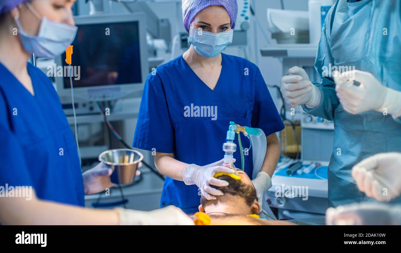 In the Hospital Operating Room Anesthesiologist Applies Anesthesia Mask to a Patient, Assistants
