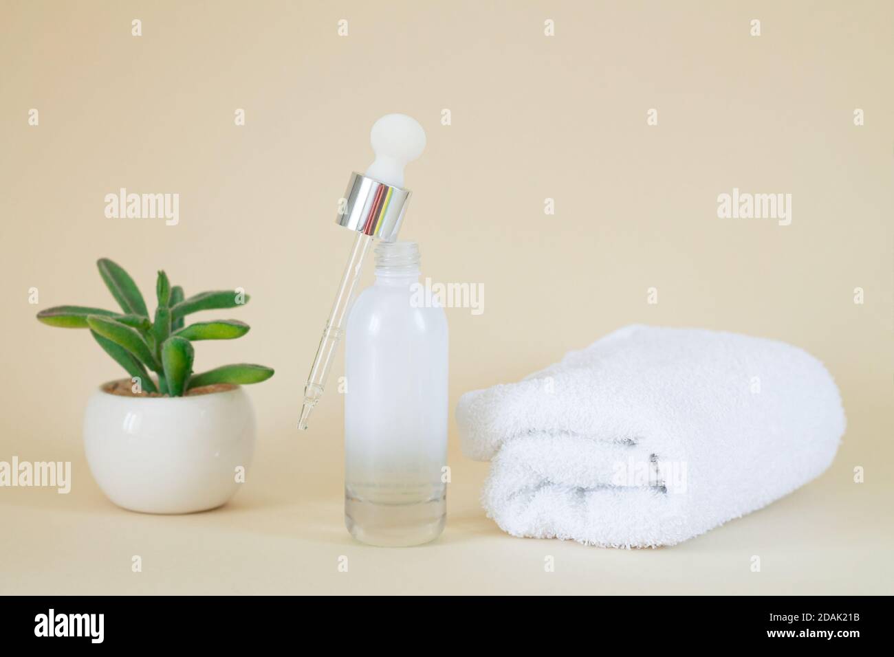 Cosmetic clear glass open serum bottle next to plant and towel Stock