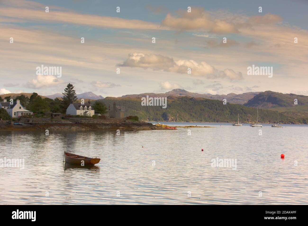 A peaceful scene in Plockton, Wester Ross. A wooden rowing boat bobs on the ebbing tide with white painted cottages on the shoreline. Stock Photo