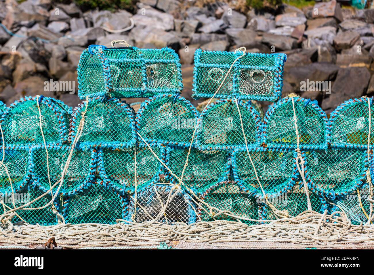 Blue lobster pots creels are neatly stacked on a jetty in the Highlands of Scotland in front of a greystone background. Two look like bad robots. Stock Photo