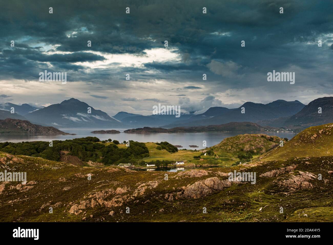 White painted cottages are dwarfed by the majesty of Loch Torridon in the North West Highlands of Scotland. Cloud adds to the ruggedness of the scene Stock Photo