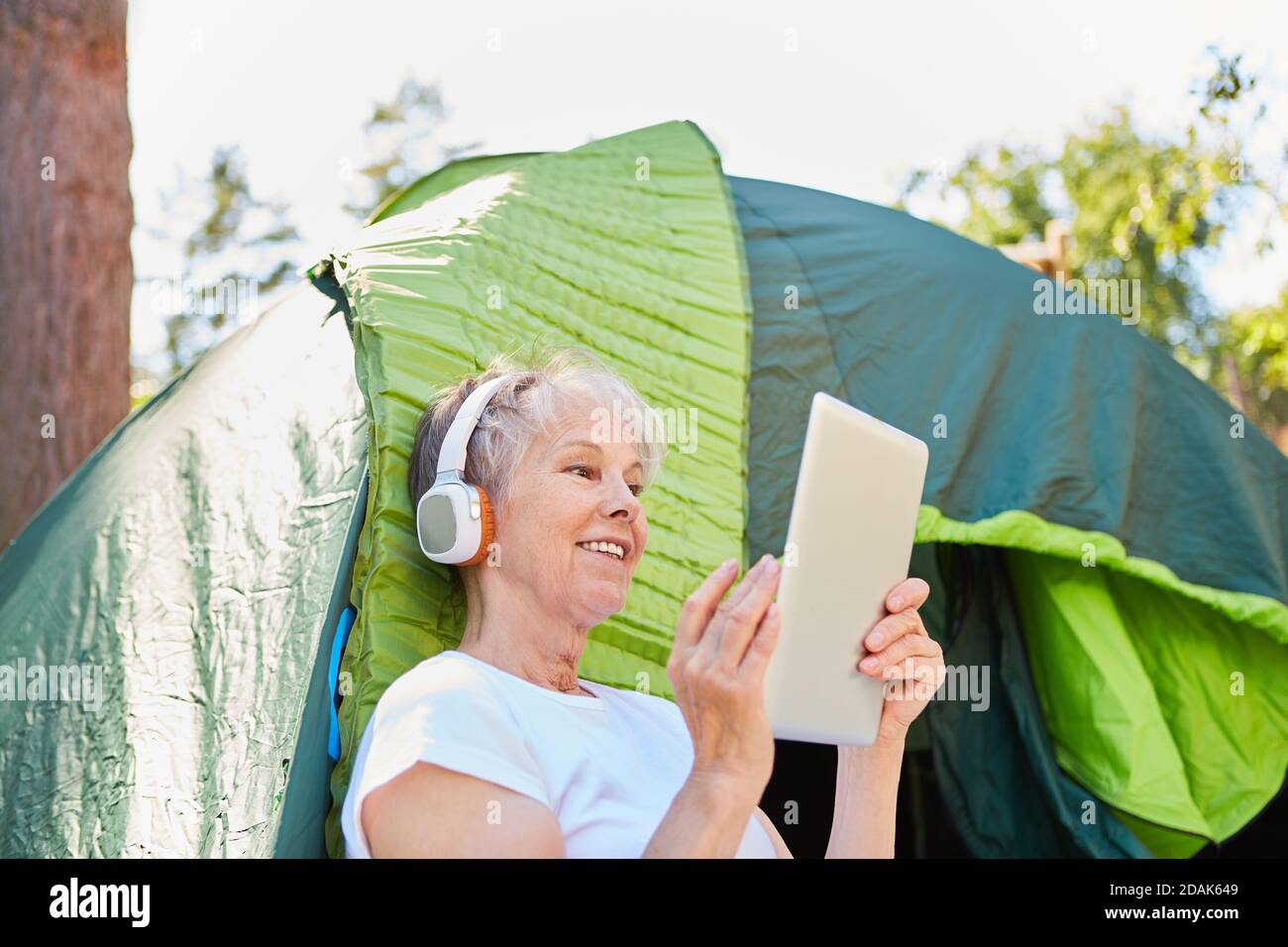 Senior woman with headphones and tablet PC in front of the tent while streaming or listening to music Stock Photo