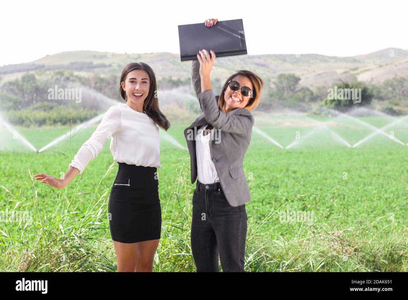 Two business women with a laptop in a field, jumping and celebrating ...