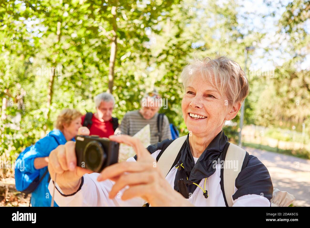 Happy elderly woman with camera in front of a hiking group in nature in ...