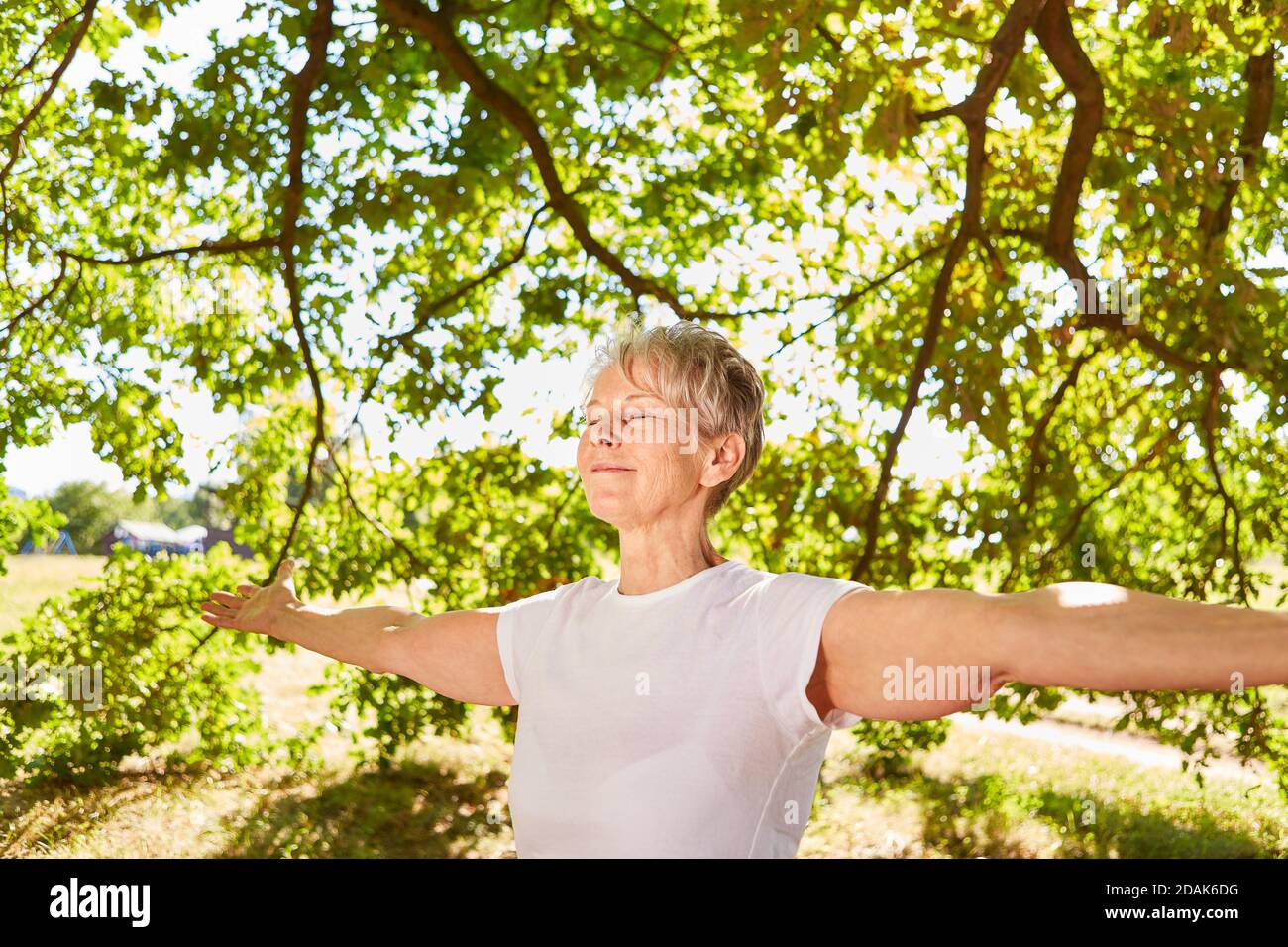 Happy elderly woman with arms outstretched doing a meditation and breathing exercise Stock Photo