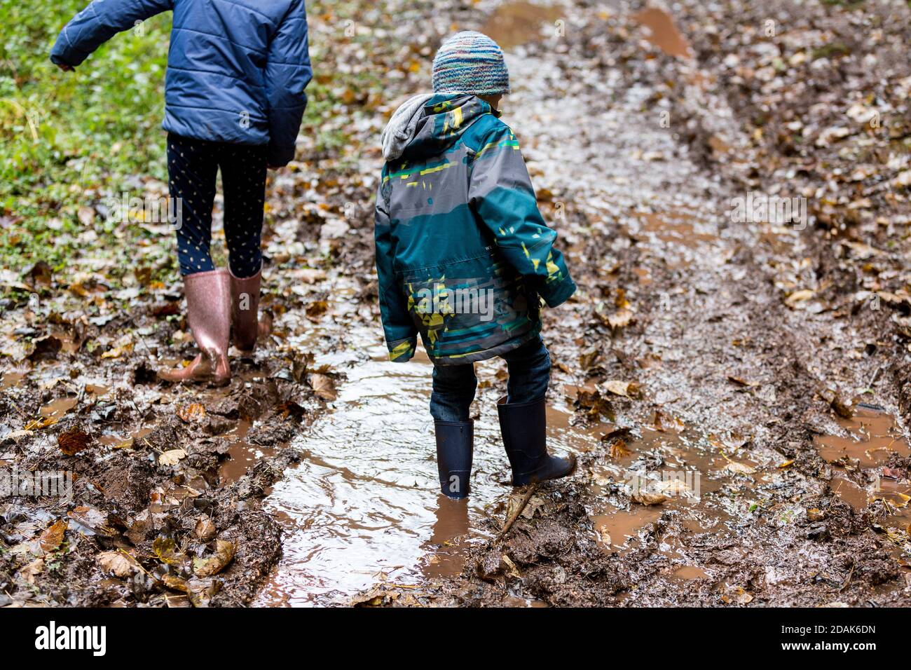 Two children wearing wellies walking through deep mud. Stock Photo