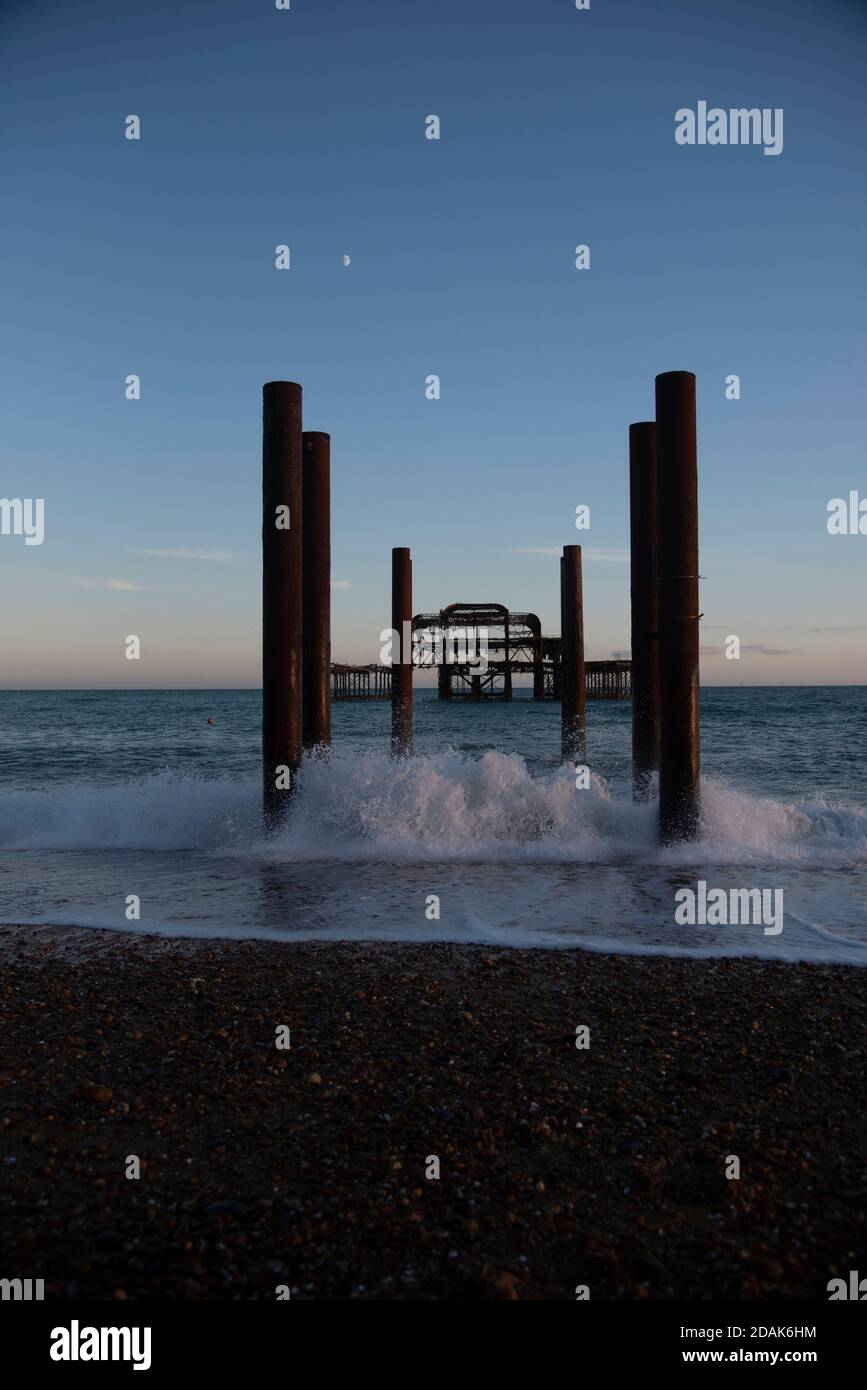 Looking directly at the remains of Brighton West Pier at sunset with a golden sky, taken in summer. Waves crashing against the remains. Brighton UK. Stock Photo