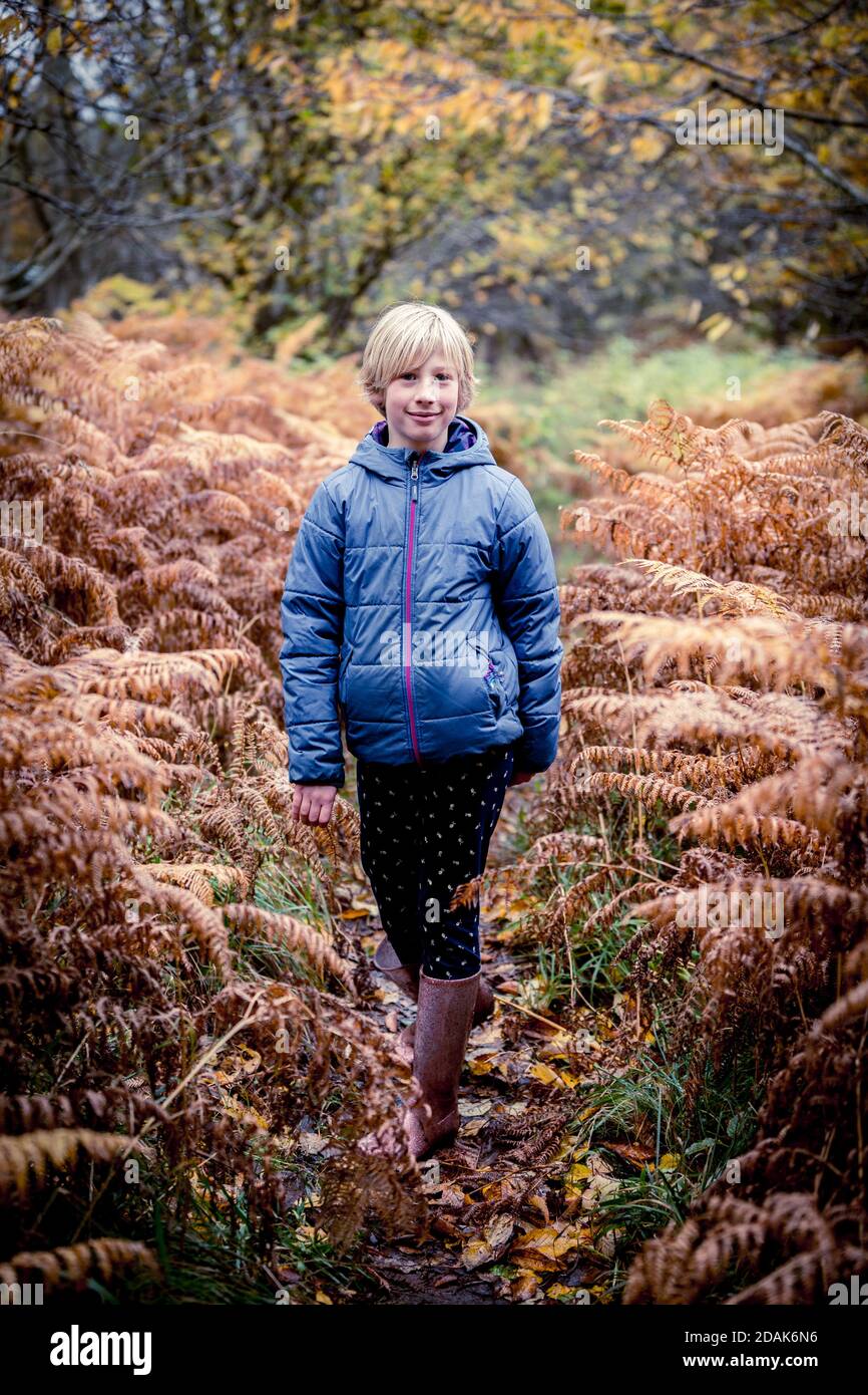 A 10 year old girl wearing wellies, on a woodland walk, surrounded by ferns. Stock Photo