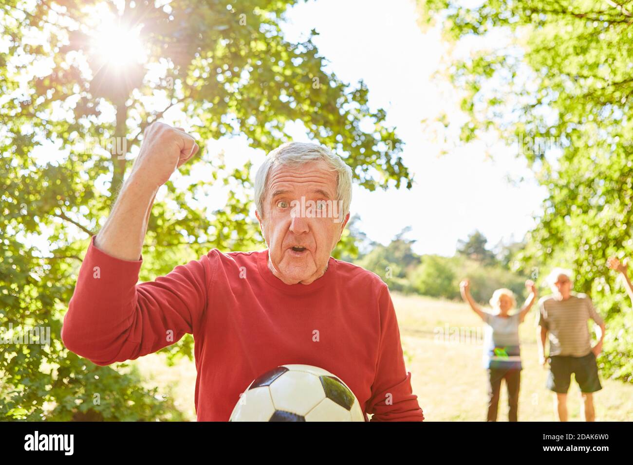 Senior as pensioner with soccer ball cheers with clenched fist after a soccer game Stock Photo