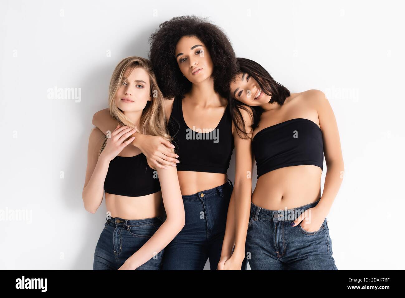 young interracial women in denim jeans and tops posing on white
