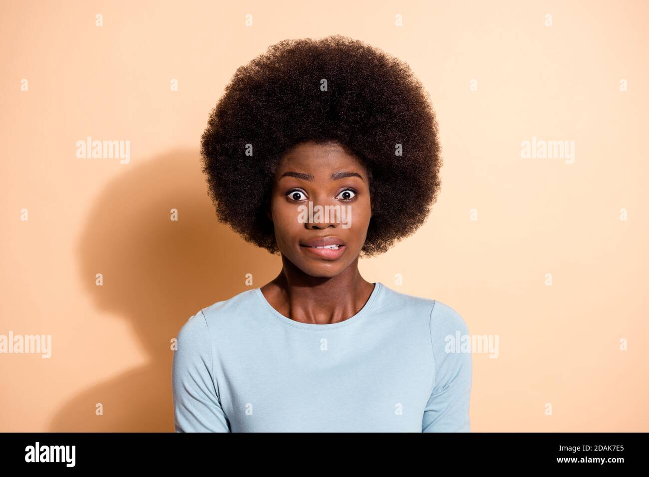 Photo portrait of nervous african american woman biting lip isolated on pastel beige colored background Stock Photo