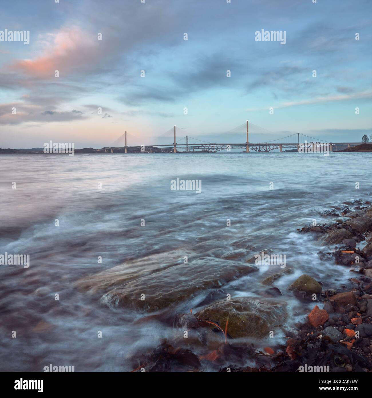 A coast of the sea bay with stones at sunset near New Queensferry Crossing Bridge in Scotland Stock Photo