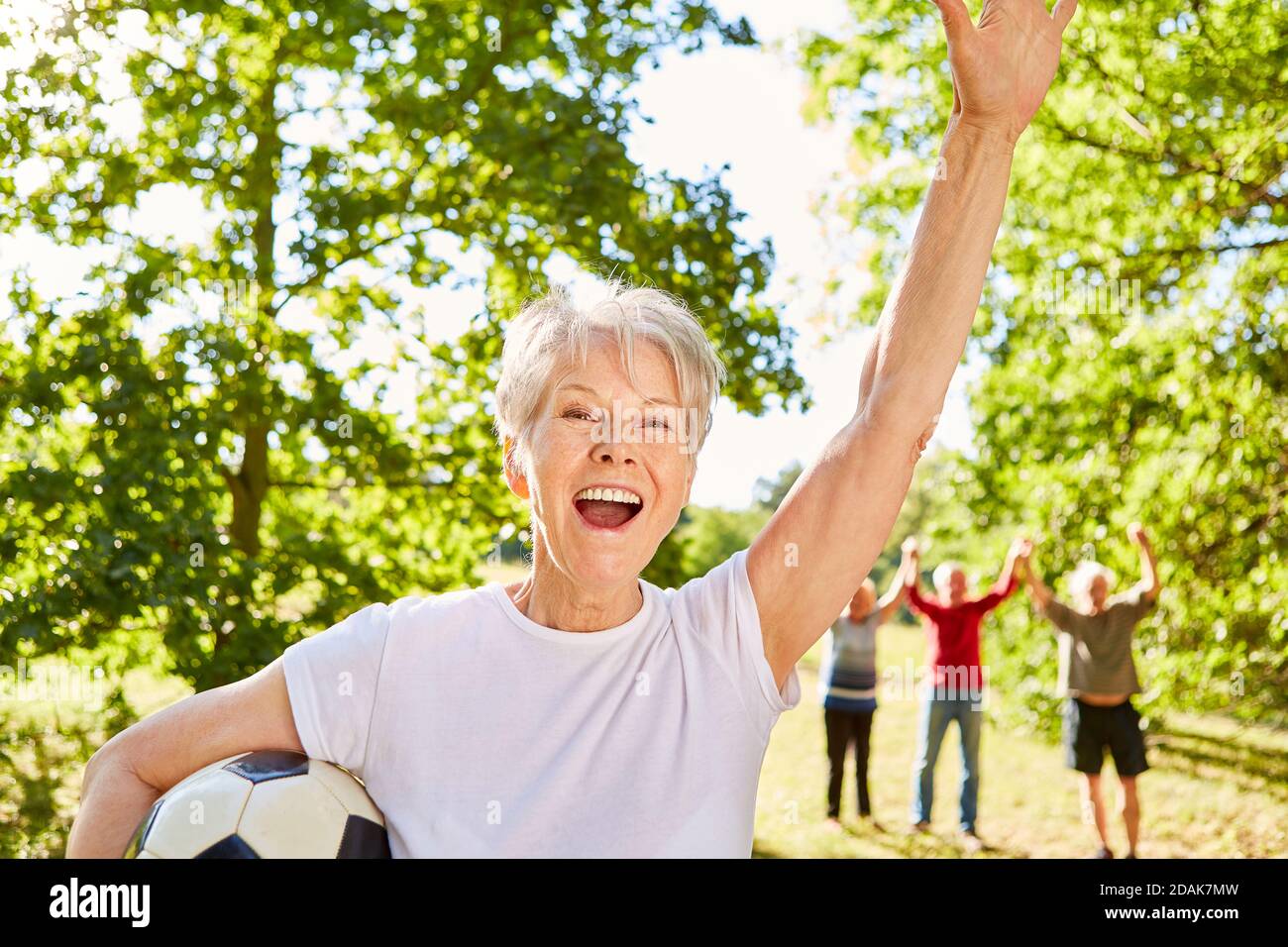 Cheering senior woman playing soccer with friends in the park in summer Stock Photo