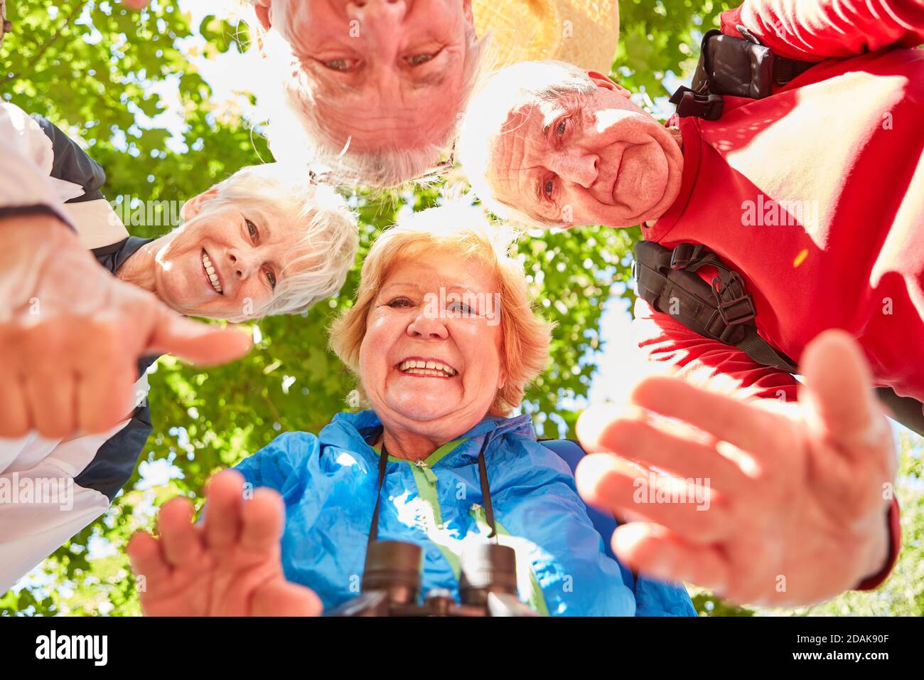 Group of active seniors in a hiking group in nature in summer beckoning happily Stock Photo