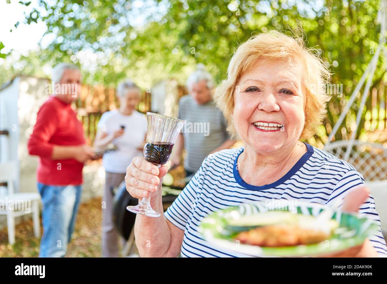 Happy elderly woman with a glass of red wine and a grill plate at a ...