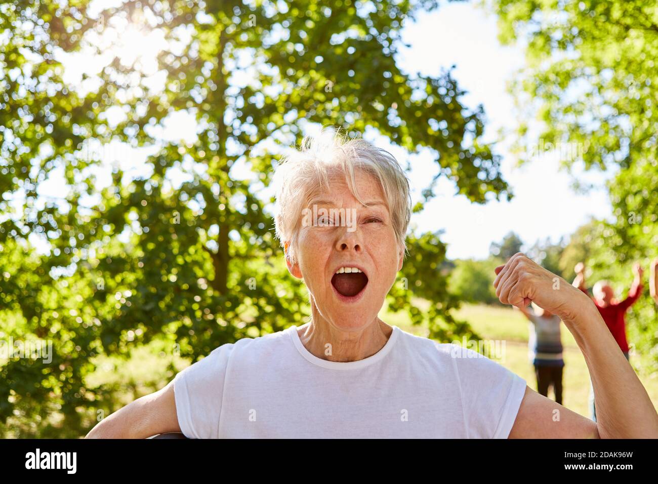 Successful senior citizen in the park at senior sport cheers with clenched fists Stock Photo