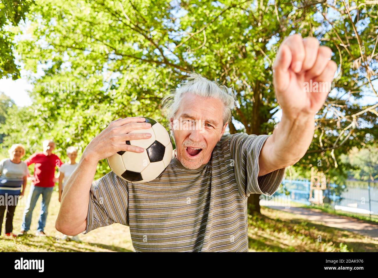 Senior man with soccer ball is happy as winner and cheers with clenched