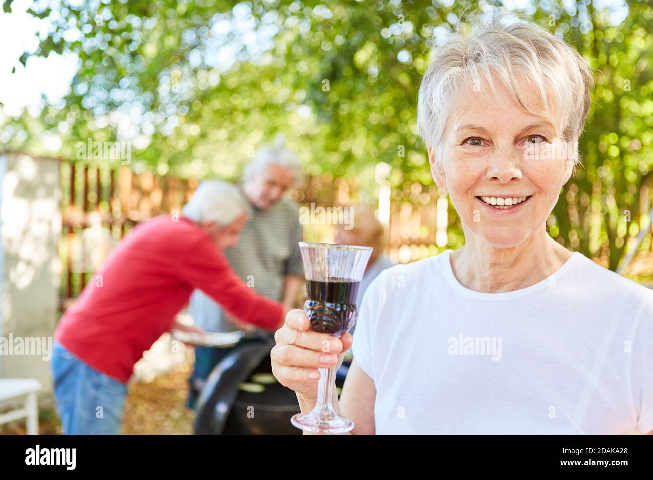 Happy elderly woman with a glass of wine at a summer garden party with ...