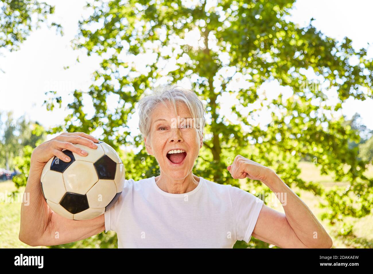 Vital senior woman with soccer ball cheers with clenched fists as the winner after a game Stock Photo
