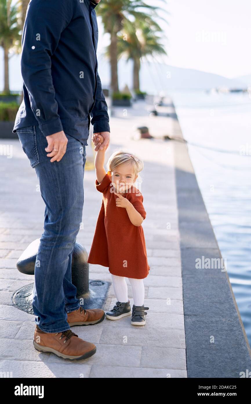 Father and daughter are walking hand in hand by the sea on a sunny day ...