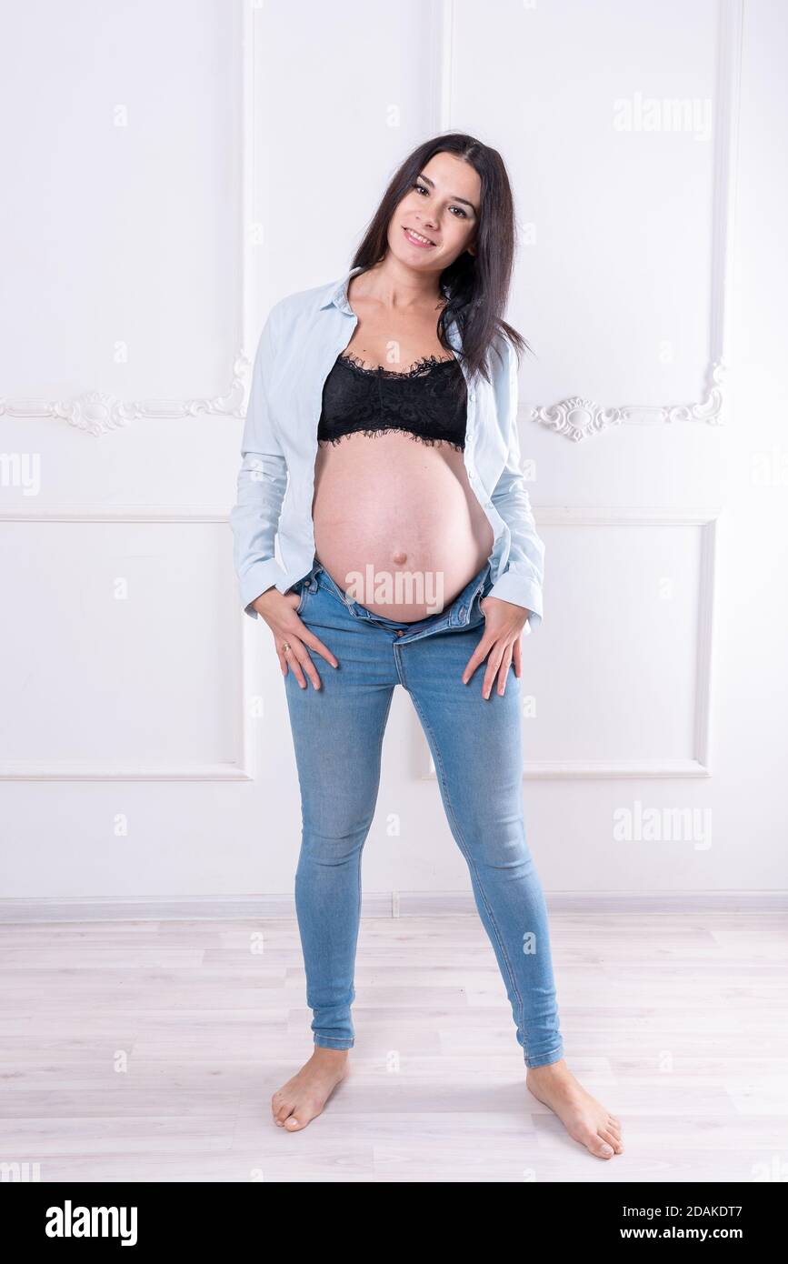 Happy pregnant girl in jeans and unbuttoned shirt Stock Photo