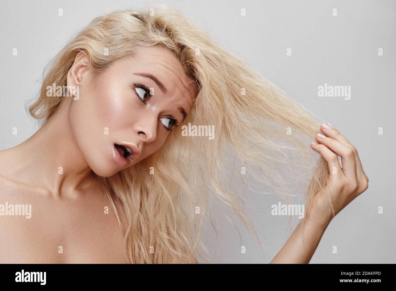 Bad hair day. Beautiful woman with messed up hair. Unhappy grimacing face. Blond bleaching hairstyle with problem brittle hair Stock Photo