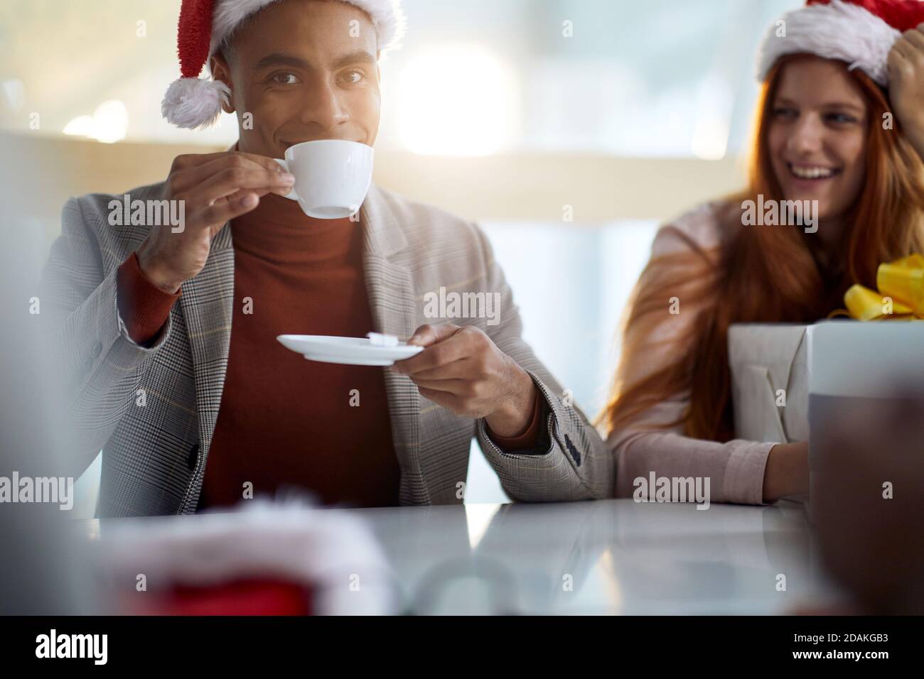 young afro-american employee drinking coffee in the office, wearing plaid jacket, turtleneck sweater and santa hat. looking at camera Stock Photo