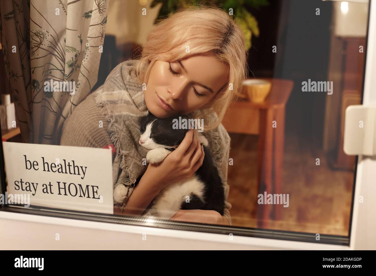 Be Healthy, Stay Home. Woman blonde in home clothing in apartment with cute cat in her arms stay at home. Self isolating while quarantine concept. Sto Stock Photo