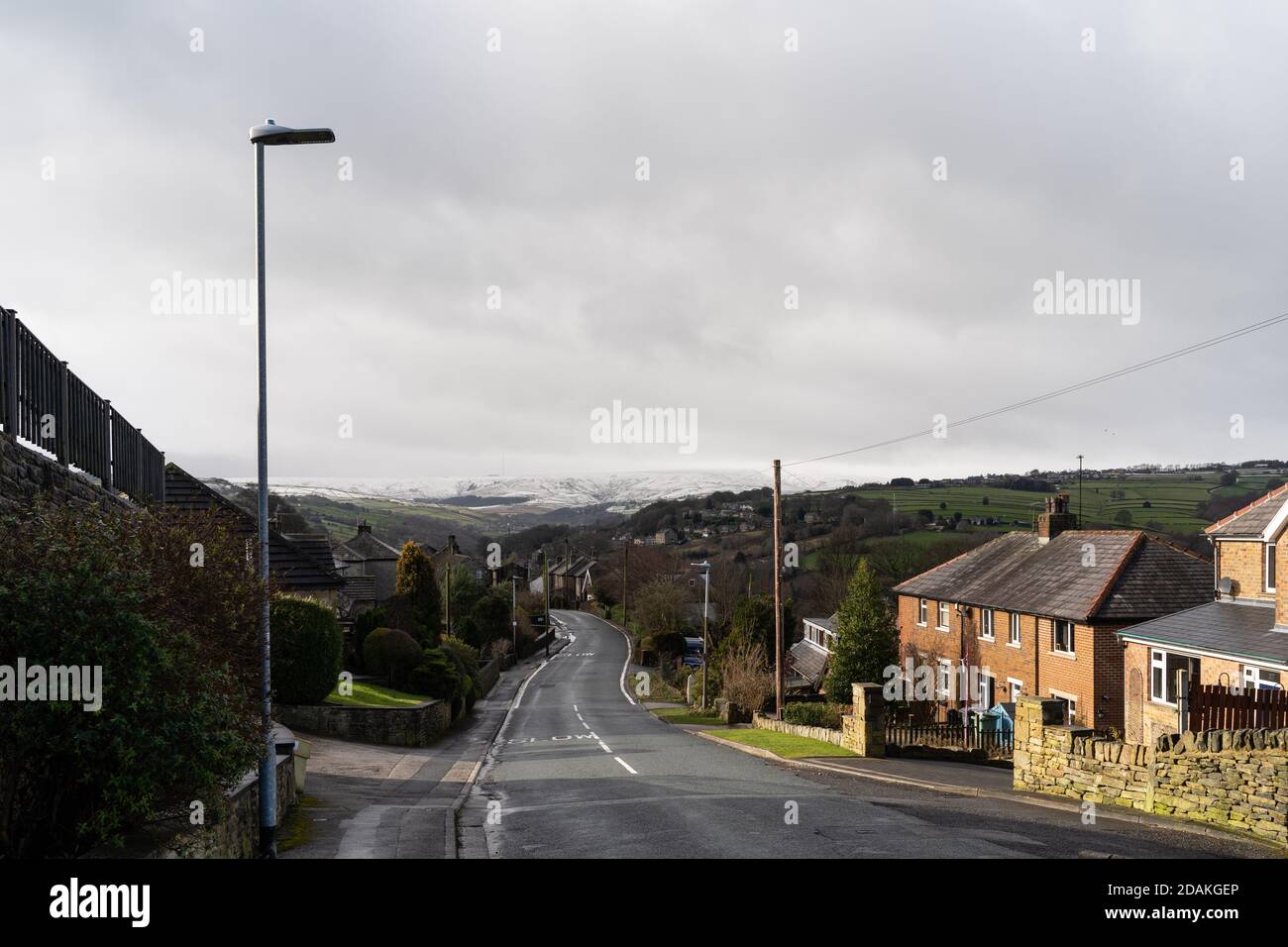 road leading down into Holmfirth with suburban houses and a snow