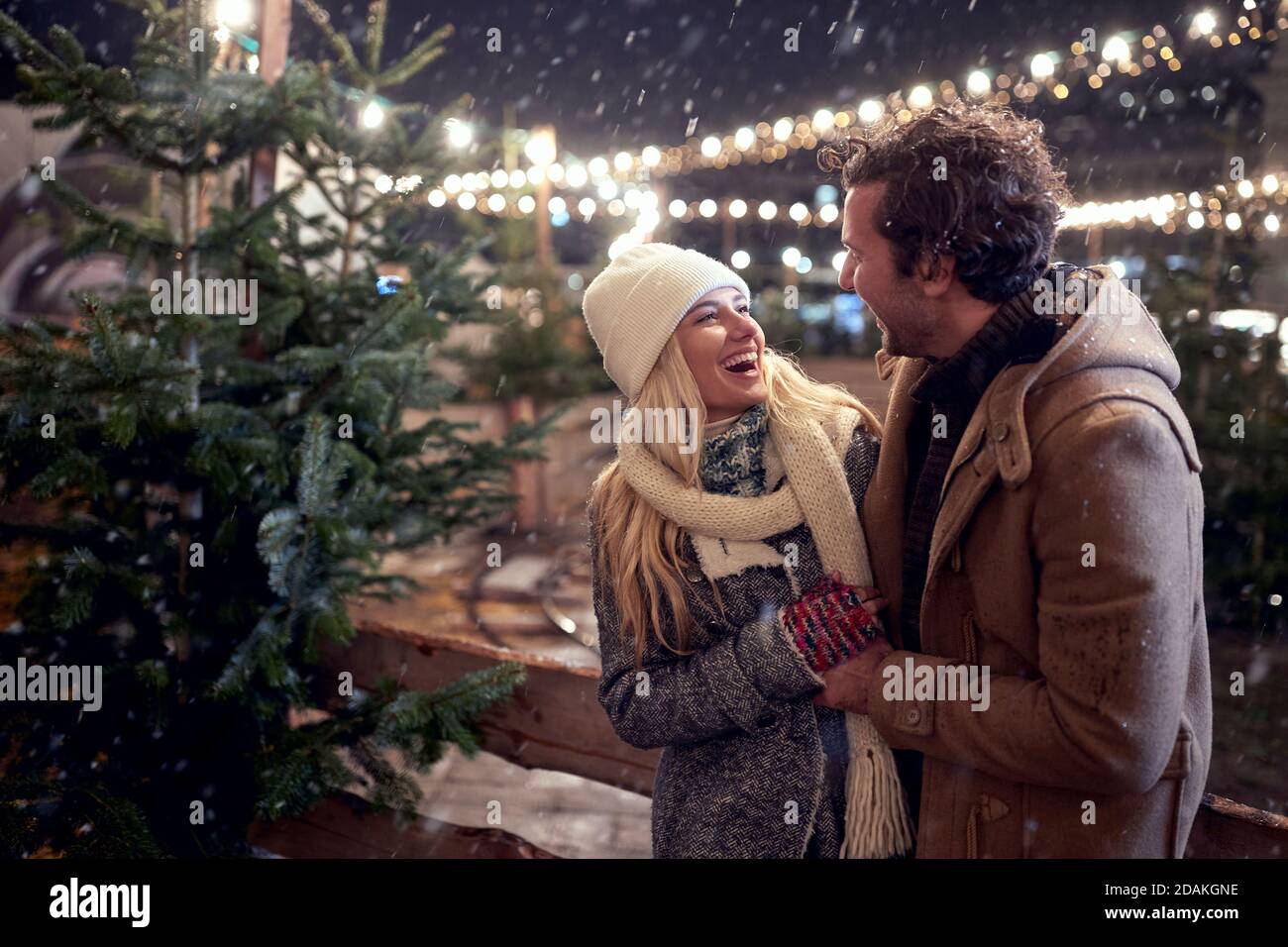 A young happy couple enjoying snowfall in a magical night in the city. Christmas tree, love, relationship, Xmas, snow Stock Photo