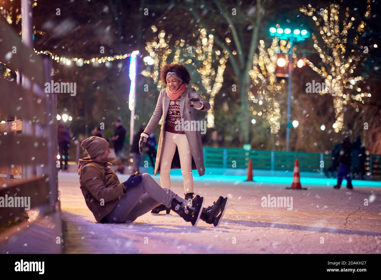 A young guy has a fall at skating on ice rink on a beautiful magical night. Skating, closeness, love, together Stock Photo