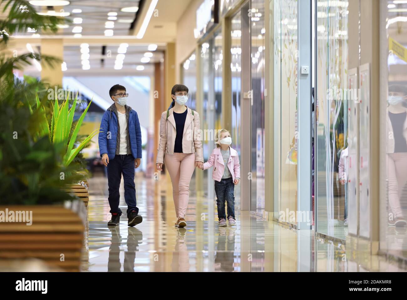 Mom, daughter and son in protective masks walk through the mall and look at the shop windows Stock Photo