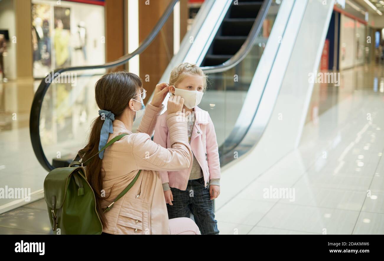Mom puts her little daughter on a face mask in the mall while shopping Stock Photo