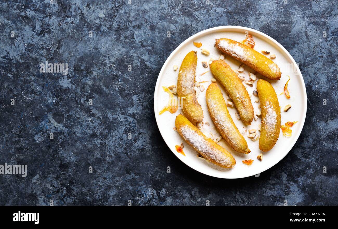 Deep fried bananas on white plate over blue stone background with free