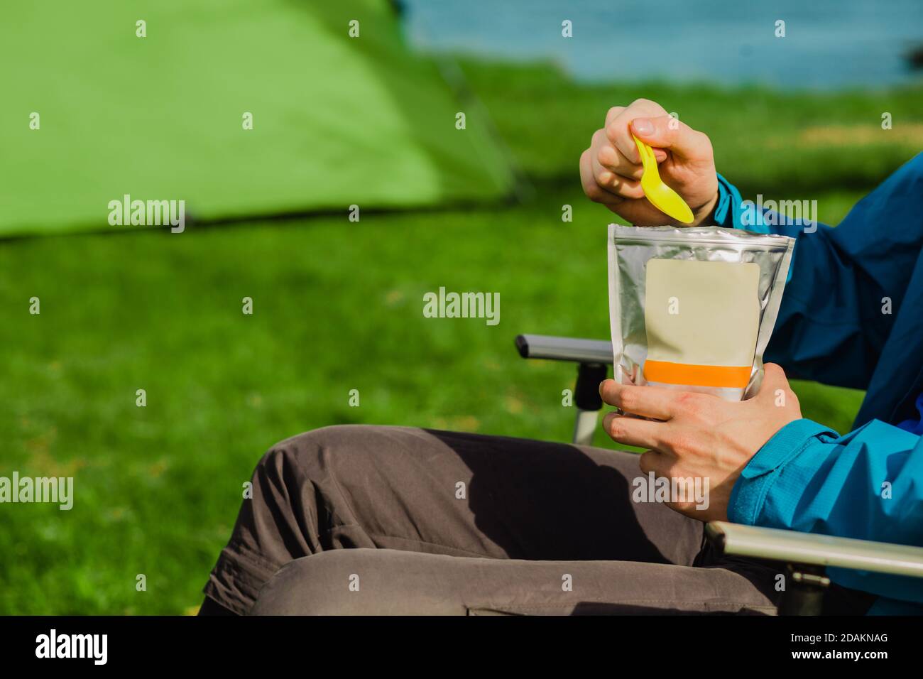 Hand holding freeze dried food ,enjoy a tasty food during the camping holidays. In the background tourist tent and equipment for outdoor activities. Stock Photo