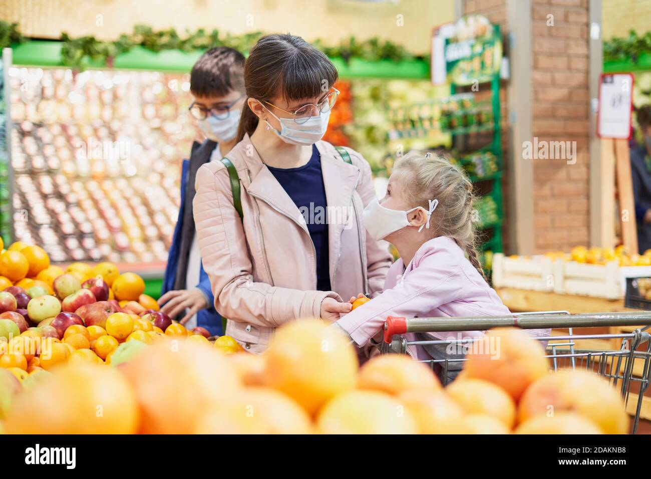 Mom with children in protective masks in a grocery store choosing fruits Stock Photo