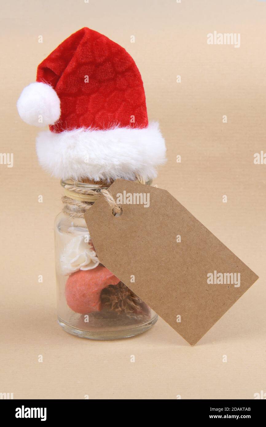Natural Christmas gift, a glass jars with dried herbs for aromatherapy wearing Santa hat with empty rectungolar tag on craft paper backrgound. Side vi Stock Photo
