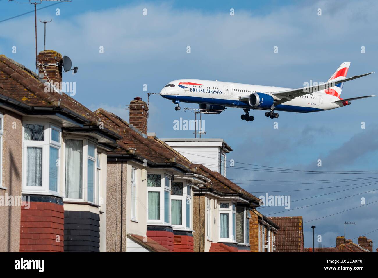 British Airways jet airliner plane on approach to land at London Heathrow Airport, UK, over roofs of homes near airport. Properties under flightpath Stock Photo